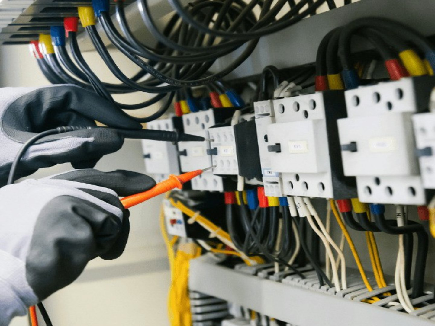 Technikerhände mit Handschuhen prüfen mit Multimeter ein Schalttafel.