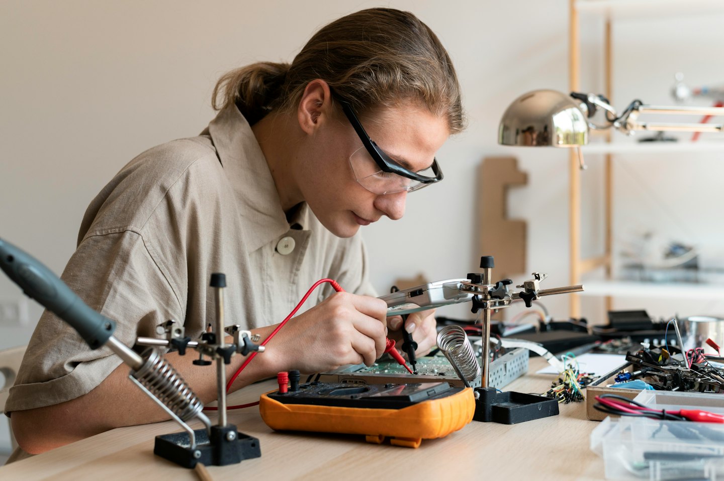 Junge Person prüft eine Platine mit einem Multimeter.